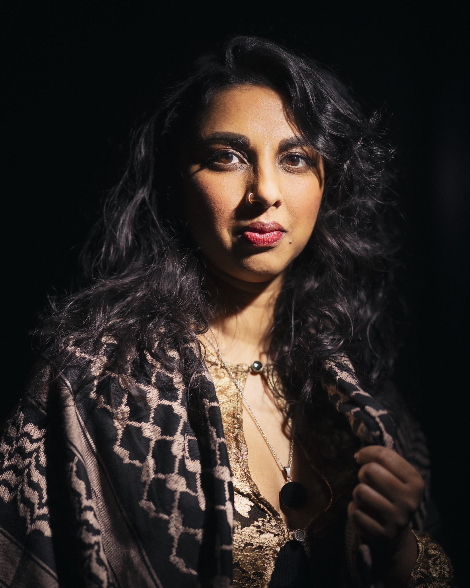 A portrait of Amirtha Kidambi. The background is black. A light shines on Amirtha Kidambi from the top right of the photo.